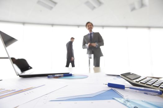 Business documents on office table with laptop and and calculator business diagram and men working in the background