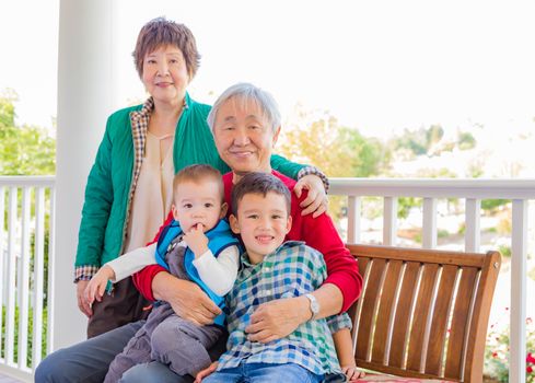 Senior Adult Chinese Couple Sitting With Their Mixed Race Grandchildren