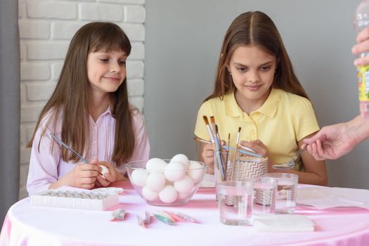 Mom prepares a solution for painting eggs, children are watching with curiosity