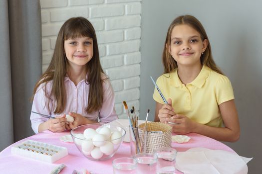 Children are preparing to paint Easter eggs while sitting at a table in a home environment.