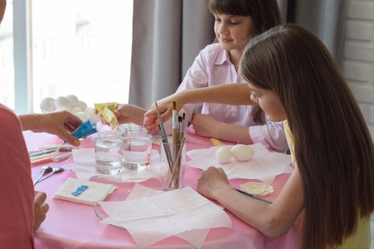 Children pour dye for coloring eggs in glasses with water