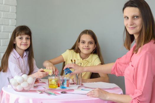 Mom and two daughters put dye in glasses with water