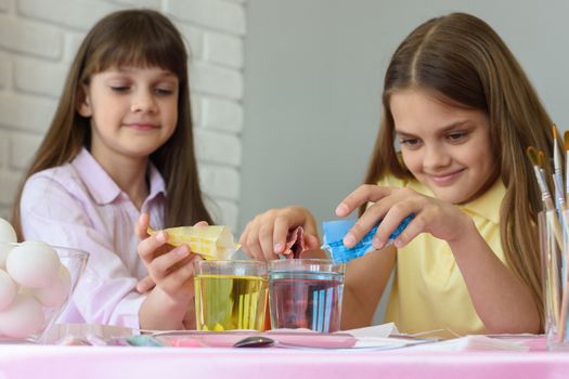 Sisters pour dye for coloring eggs in a glass of water