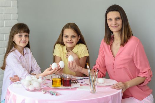 Mom and two daughters are sitting at the table preparing eggs for Easter and looked in the frame