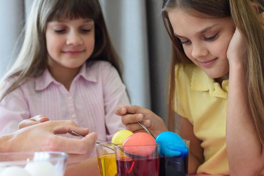 Children paint chicken eggs in different colors.