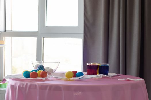 Table with colorful Easter eggs and dyes in the interior of the room by the window