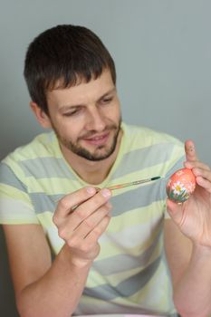 Man paints an Easter egg with a brush