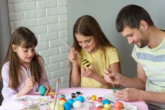 Dad with two daughters paint eggs for Easter holiday