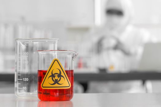 Beaker contains red liquid chemicals on a white laboratory table.