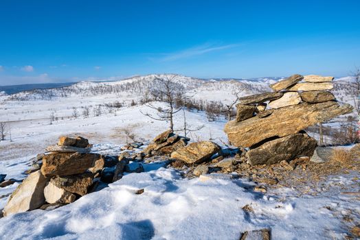 Strange shaped rocks arranged in vertical rows. The morning atmosphere on the top of the snow-capped mountains of Kurkutsky Bay. Lake Baikal, Russia.