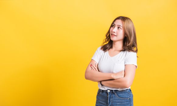 Asian Thai happy portrait beautiful cute young woman standing wear t-shirt her smile confidence with crossed arms looking to side up isolated, studio shot on yellow background and copy space