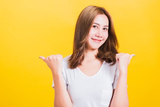 Portrait Asian Thai beautiful happy young woman smiling wear white t-shirt standing successful woman giving two thumbs up gesture sign in studio shot, isolated on yellow background with copy space