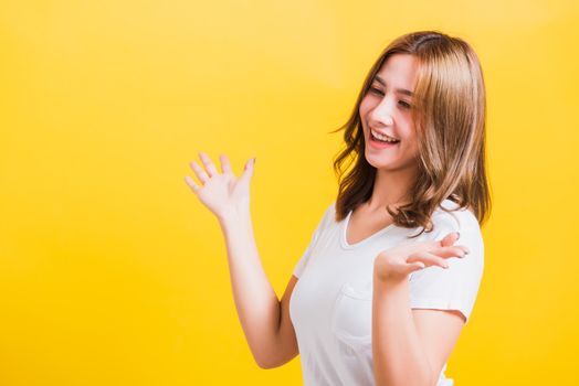 Asian Thai happy portrait beautiful cute young woman standing wear t-shirt her winning and surprised excited screaming open mouth showing hands, studio shot isolated yellow background with copy space