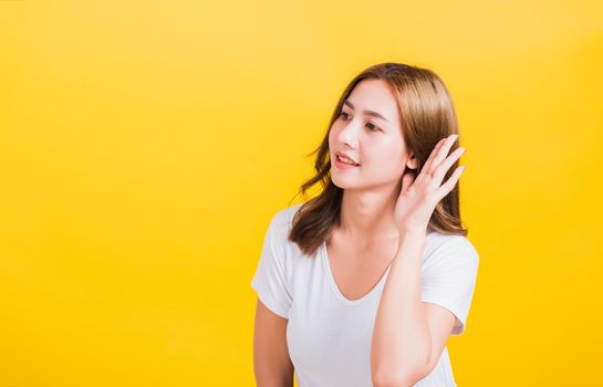 Portrait Asian Thai beautiful young woman listening something with her palm hand behind the ear, studio shot isolated on yellow background, There was copy space, Gossip concept