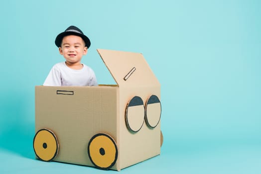 Happy Asian children boy smile in driving play car creative by a cardboard box imagination, summer holiday travel concept, studio shot on blue background with copy space for text