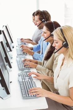 Side view of young business people with headsets using computers in office