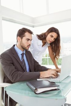 Two young business people using laptop in office