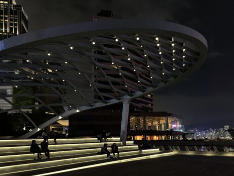 The silhouette of people sitting on staircases under modern building with Hong Kong city at nighttime 