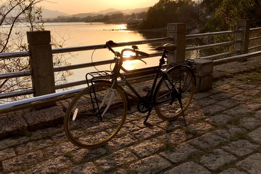 The retro bicycle, metal fence, stone floor and lake at sunset