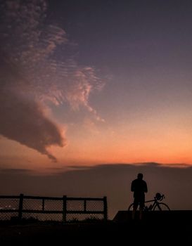 The silhouette of bicycle, rider and wooden fence with gradient sky at sunset