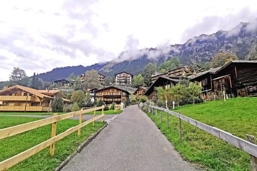 The outdoor countryside house building, mountain, green field, footpath with wooden fence in Switzerland