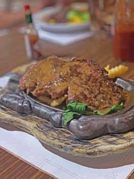 The vertical cooked steak meat with vegetable, french fries on the metal dish