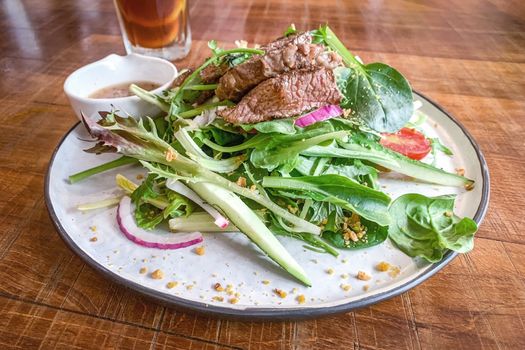 The roasted beef onion vegetable healthy salad on white dish and wooden table