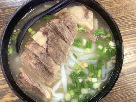 The black bowl of Chinese food meat noodles on wooden table