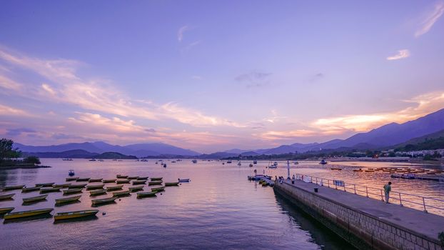 Recreational and fishing boats are parked on lake near countryside pier at sunset
