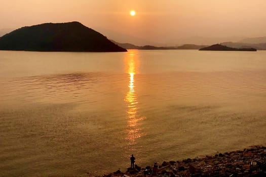 The silhouette of fishing man, ocean, mountain and sun at sunset