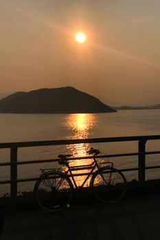 The silhouette of retro bicycle, fence, ocean, mountain and sun at sunset