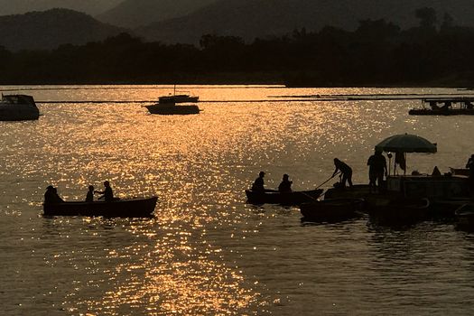 The silhouette of recreational boat on the park lake at orange sunset