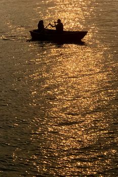 The silhouette of dating couple and recreational boat on the park lake at orange sunset