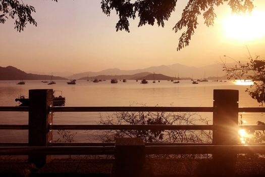 The silhouette of fence, tree, mountain, boat and ocean at sunset