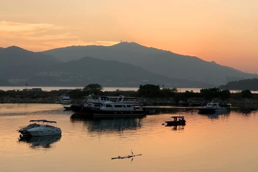 Fishing boats with water reflection in wharf and gradient orange sky at sunset