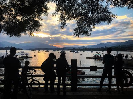 The silhouette of people, bicycle, boat and the pier at sunset