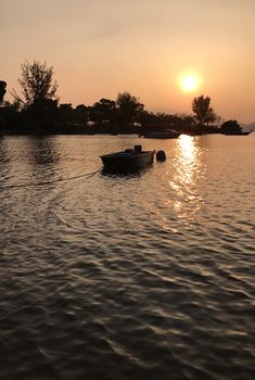 Sun, tree and fishing boat on the lake at the sunset