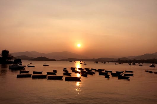 The silhouette of fishing boat on lake with sun and mountain at sunset