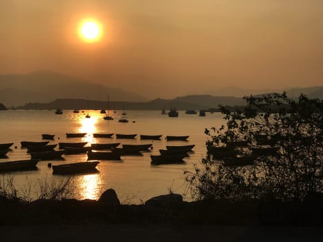 The silhouette of fishing boat on lake with sun and mountain at sunset