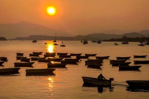 The silhouette of fishing boat on lake with sun and mountain at sunset