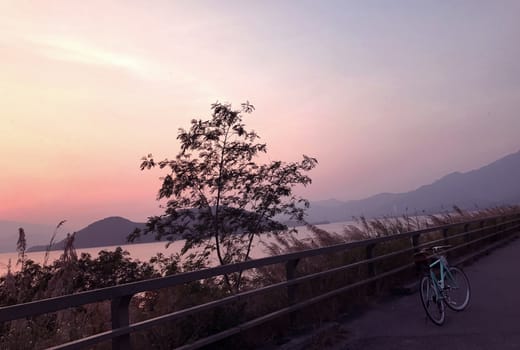 Mint green retro bicycle, road frame, mountain, lake and gradient sky at sunset