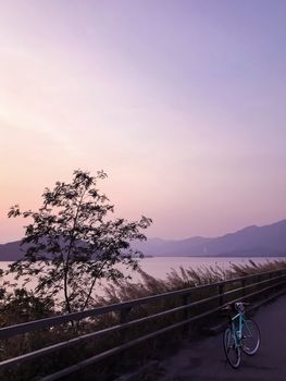 Mint green retro bicycle, road frame, mountain, lake and gradient sky at sunset