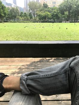 The vertical human leg, outdoor wooden floor and green field in city public park