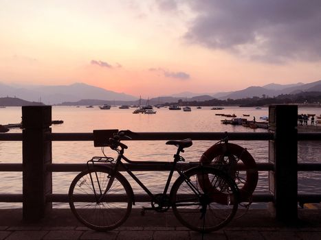 The silhouette of bicycle, fence and sea at sunset