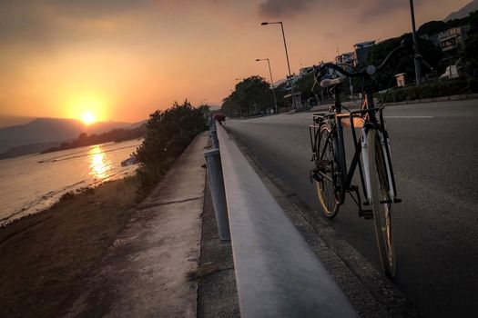 The silhouette of bicycle, fence, road and sea at sunset