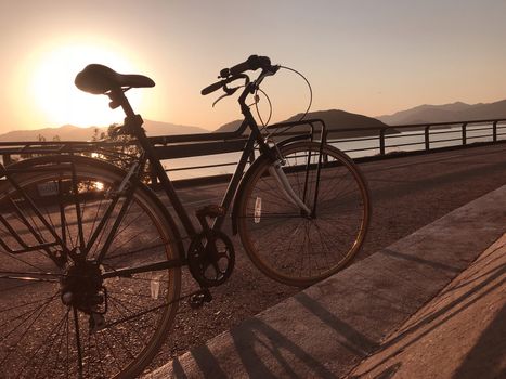 The silhouette of bicycle, fence, road and sea at sunset
