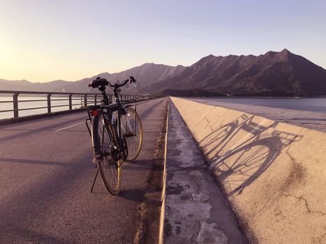 The silhouette of bicycle, fence, road and sea at sunset