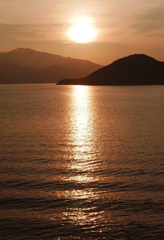 Vertical sun, mountain, ocean and water wave at sunset