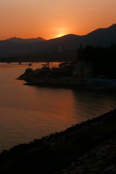 Vertical silhouette of boats, sun, mountain and sea at sunset