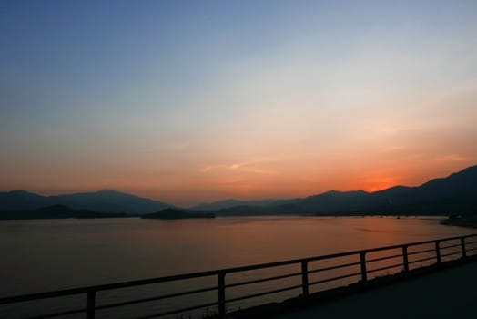 footpath, fence, sea, lake and mountain at sunset